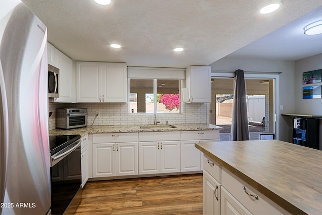 kitchen with white cabinetry, stainless steel appliances, sink, and light hardwood / wood-style flooring