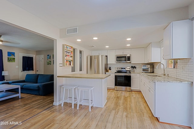 kitchen featuring appliances with stainless steel finishes, white cabinetry, sink, a breakfast bar area, and light wood-type flooring