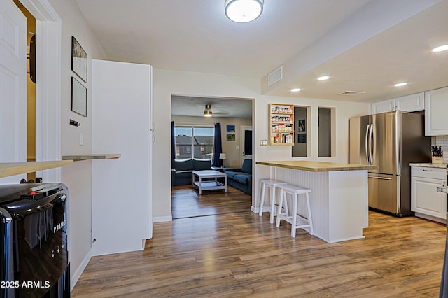 kitchen featuring stainless steel fridge, a breakfast bar, white cabinetry, hardwood / wood-style floors, and kitchen peninsula