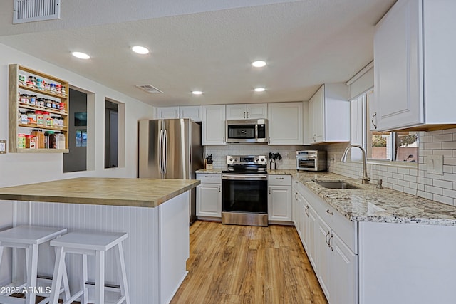 kitchen featuring appliances with stainless steel finishes, a breakfast bar, sink, white cabinets, and light hardwood / wood-style floors