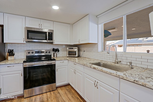 kitchen with white cabinetry, appliances with stainless steel finishes, light hardwood / wood-style floors, and sink