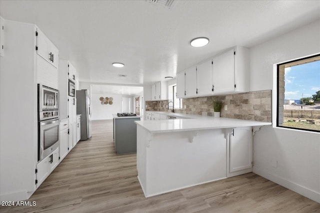 kitchen with appliances with stainless steel finishes, white cabinetry, decorative backsplash, kitchen peninsula, and light wood-type flooring