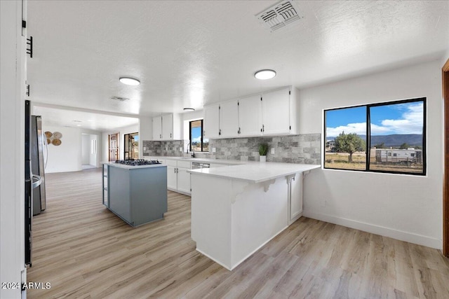 kitchen with appliances with stainless steel finishes, backsplash, white cabinets, a kitchen bar, and kitchen peninsula