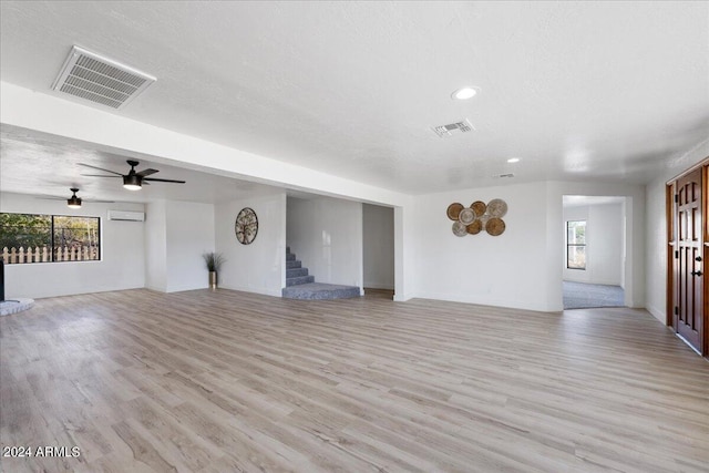 unfurnished living room featuring ceiling fan, a wall unit AC, a textured ceiling, and light hardwood / wood-style flooring