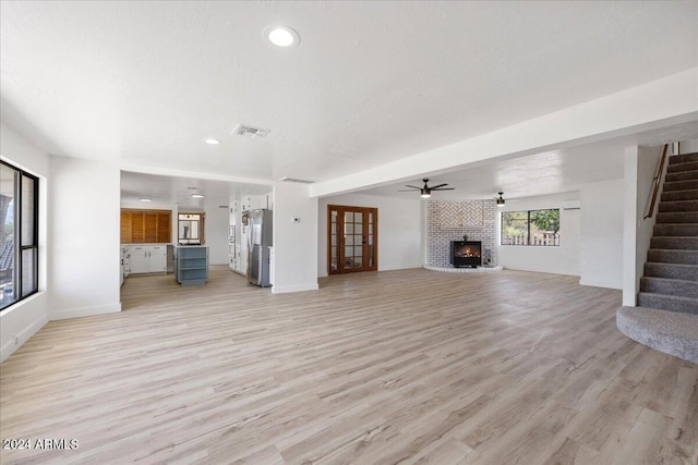 unfurnished living room with ceiling fan, a brick fireplace, a textured ceiling, and light hardwood / wood-style floors