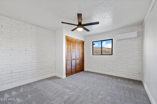 unfurnished bedroom featuring a textured ceiling, carpet floors, a closet, a wall unit AC, and brick wall