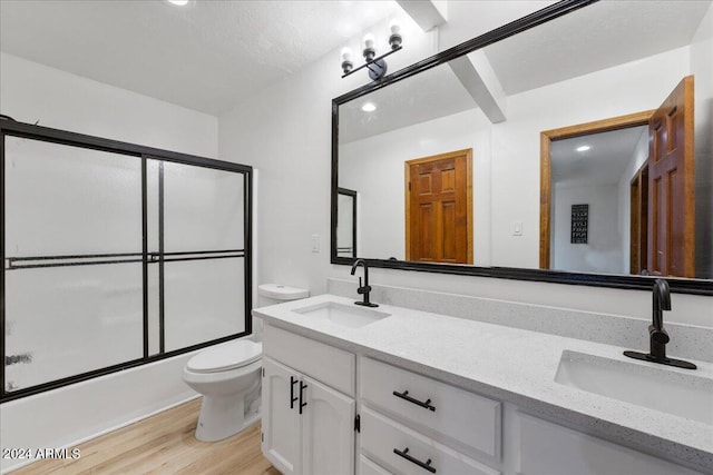 full bathroom with bath / shower combo with glass door, hardwood / wood-style floors, vanity, and toilet