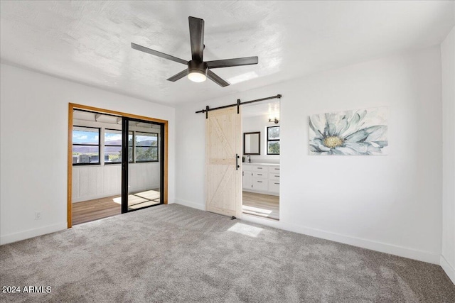 unfurnished bedroom featuring ensuite bathroom, carpet flooring, ceiling fan, a barn door, and a textured ceiling