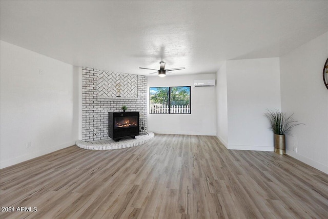 unfurnished living room featuring ceiling fan, a wall mounted air conditioner, a fireplace, and light hardwood / wood-style flooring