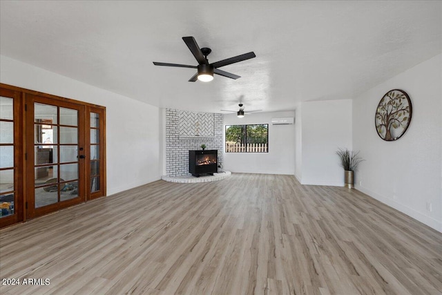 unfurnished living room with ceiling fan, a wall unit AC, a fireplace, and light hardwood / wood-style floors