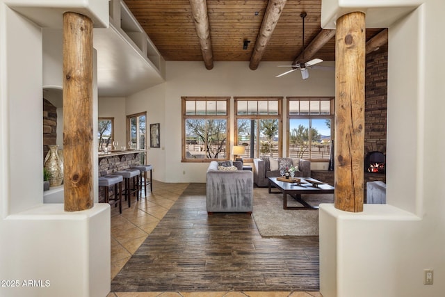 living room with wood finished floors, a ceiling fan, a high ceiling, wooden ceiling, and beamed ceiling