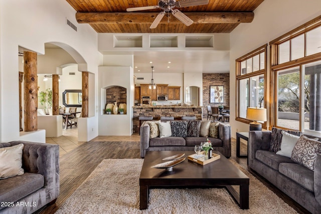 living area featuring visible vents, beam ceiling, arched walkways, wooden ceiling, and ceiling fan