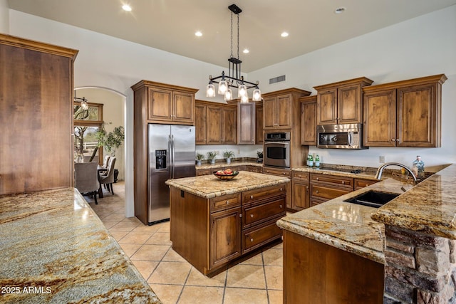 kitchen featuring a sink, light stone counters, a center island, stainless steel appliances, and arched walkways