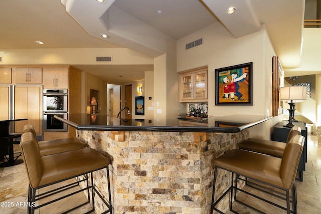 bar with light brown cabinets, stainless steel double oven, and paneled built in fridge