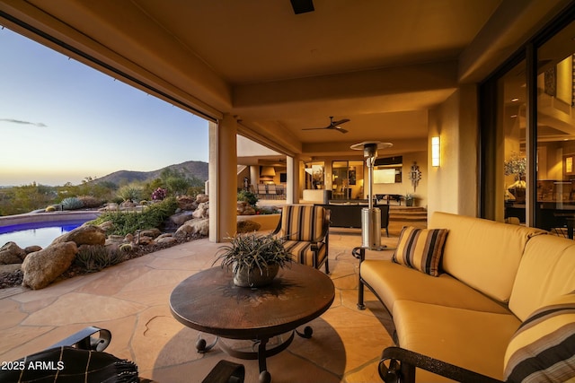 patio terrace at dusk with an outdoor living space, ceiling fan, and a mountain view