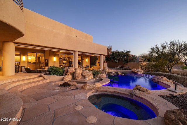 pool at dusk featuring an in ground hot tub and a patio area