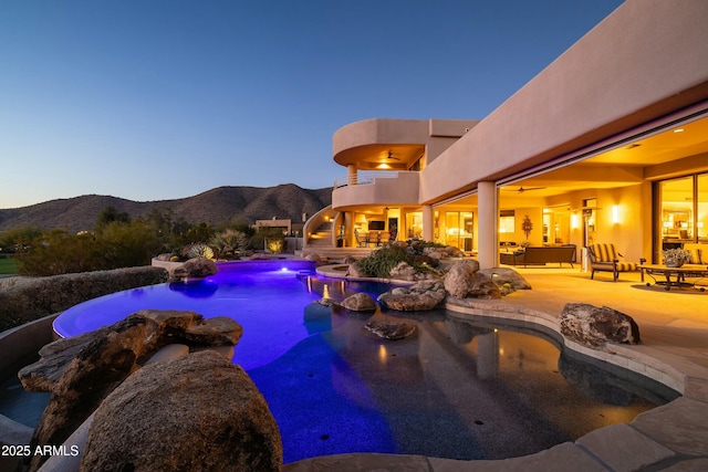 pool at dusk with a mountain view, an outdoor hangout area, ceiling fan, and a patio area