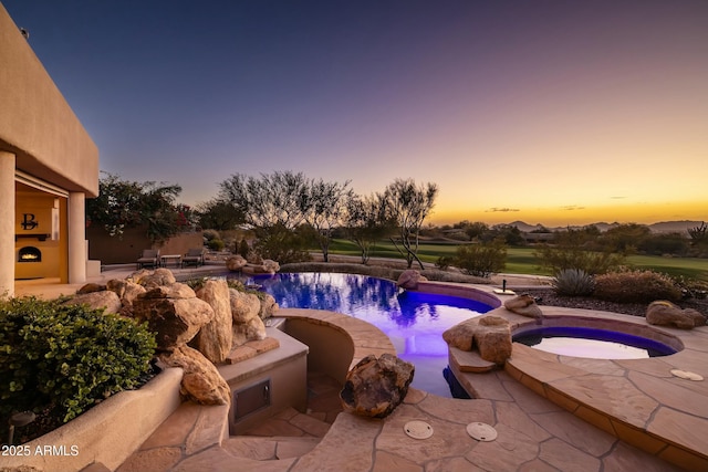 pool at dusk featuring an in ground hot tub