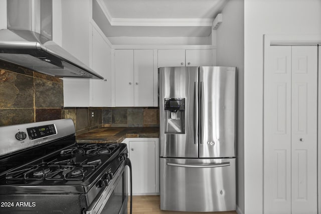 kitchen with backsplash, wall chimney range hood, ornamental molding, appliances with stainless steel finishes, and white cabinetry