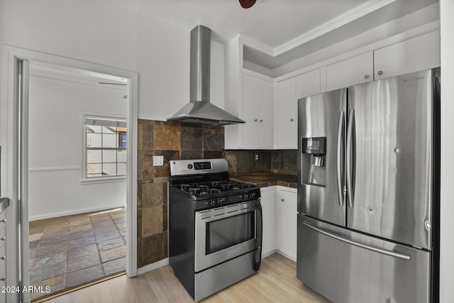 kitchen featuring wall chimney exhaust hood, appliances with stainless steel finishes, decorative backsplash, white cabinets, and ornamental molding