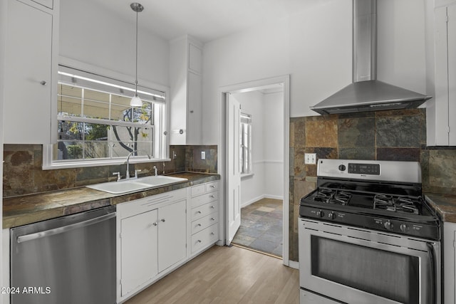 kitchen with sink, wall chimney exhaust hood, appliances with stainless steel finishes, decorative light fixtures, and white cabinetry