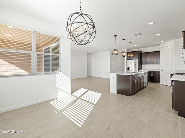 kitchen with a chandelier, an island with sink, pendant lighting, dark brown cabinetry, and sink