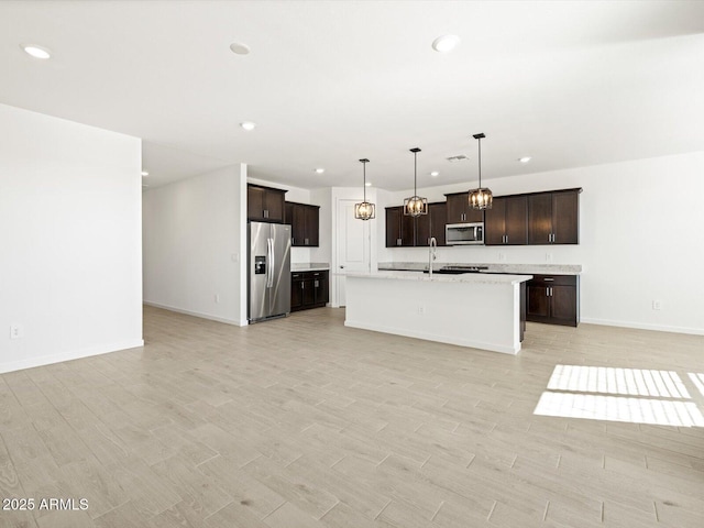 kitchen with stainless steel appliances, sink, pendant lighting, dark brown cabinets, and a kitchen island with sink