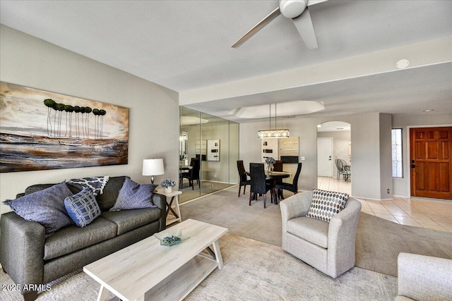 living area featuring arched walkways, ceiling fan, light tile patterned flooring, and light colored carpet