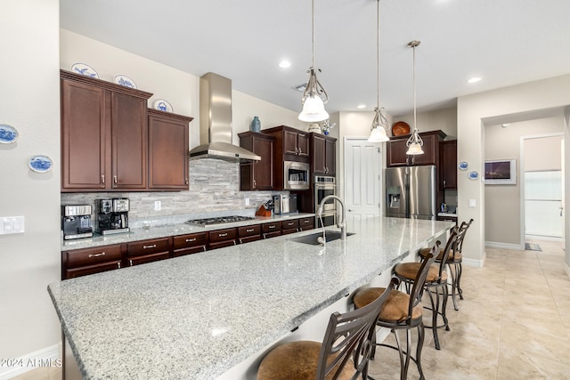 kitchen featuring stainless steel appliances, sink, wall chimney range hood, a spacious island, and pendant lighting