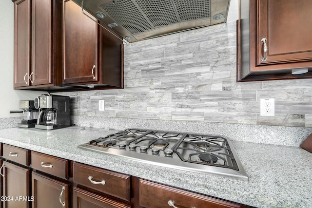 kitchen featuring ventilation hood, backsplash, light stone countertops, and stainless steel gas cooktop