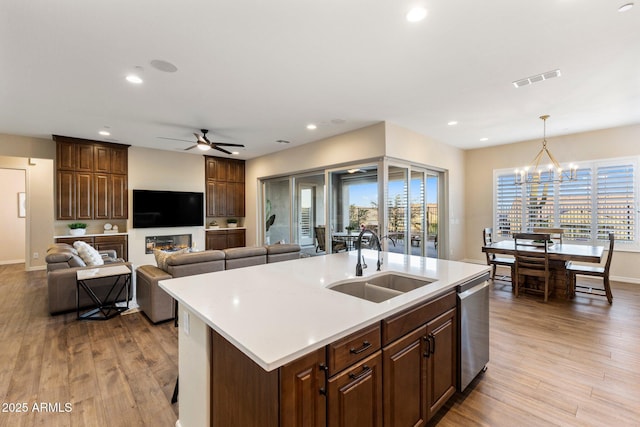 kitchen featuring dishwasher, a sink, open floor plan, light countertops, and ceiling fan with notable chandelier