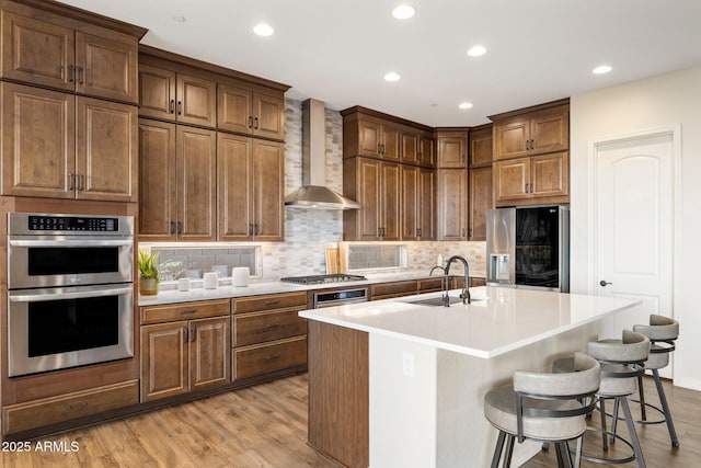 kitchen featuring tasteful backsplash, wall chimney range hood, appliances with stainless steel finishes, and light wood finished floors