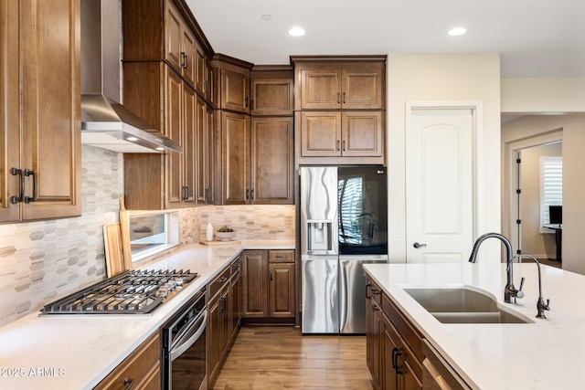 kitchen featuring light countertops, wall chimney exhaust hood, a sink, and appliances with stainless steel finishes