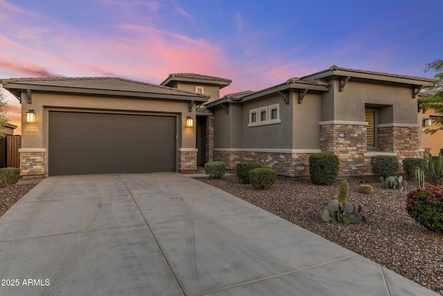 prairie-style house featuring concrete driveway, stucco siding, stone siding, an attached garage, and a tile roof