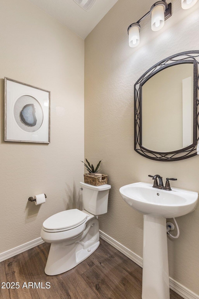 half bath with baseboards, toilet, and wood finished floors