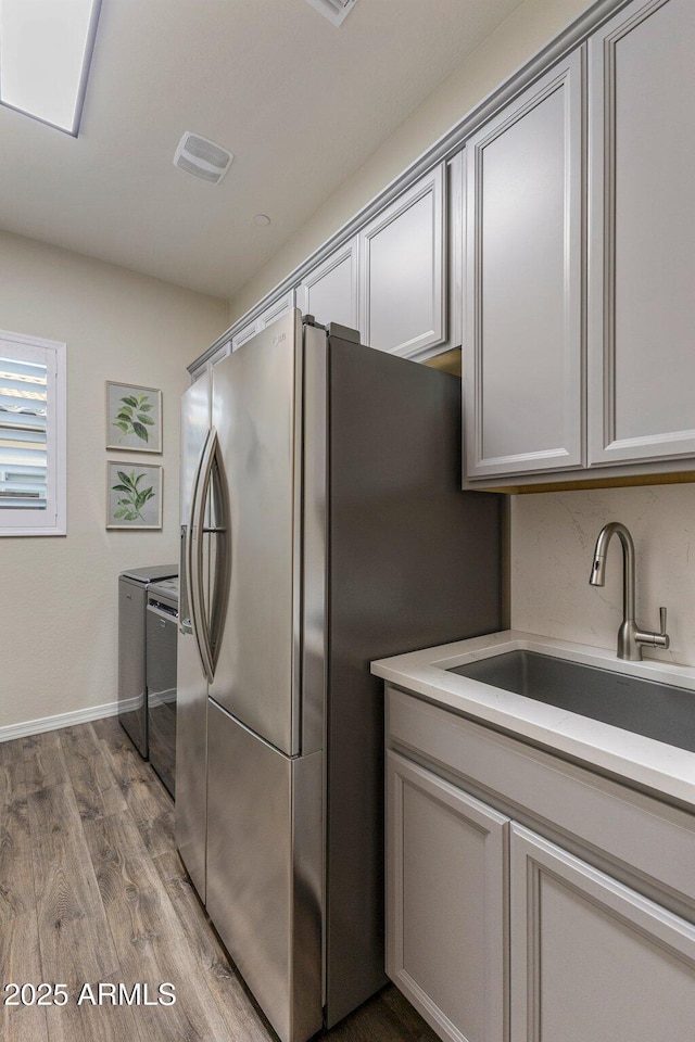 kitchen featuring stainless steel fridge with ice dispenser, dark wood-style flooring, light countertops, visible vents, and a sink