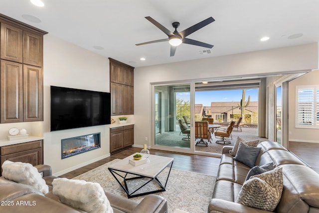 living area featuring ceiling fan, dark wood finished floors, a glass covered fireplace, visible vents, and recessed lighting