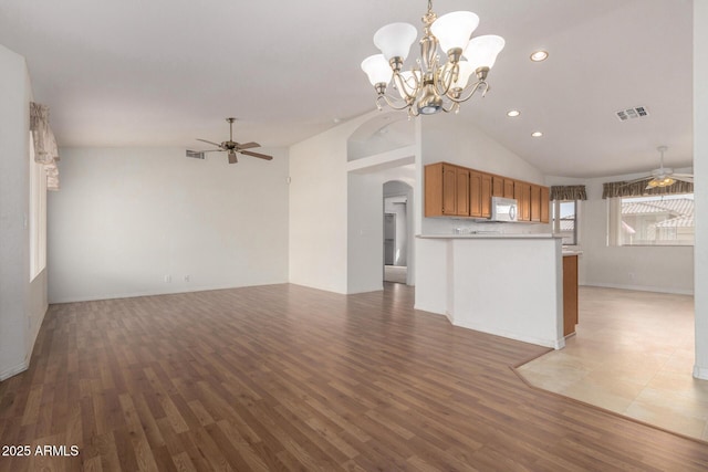 kitchen with arched walkways, white microwave, ceiling fan with notable chandelier, open floor plan, and light wood finished floors