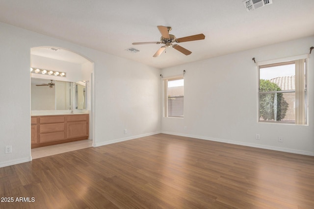 unfurnished bedroom with baseboards, visible vents, wood finished floors, and ensuite bathroom