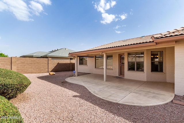 rear view of property with a patio, brick siding, a tile roof, and fence