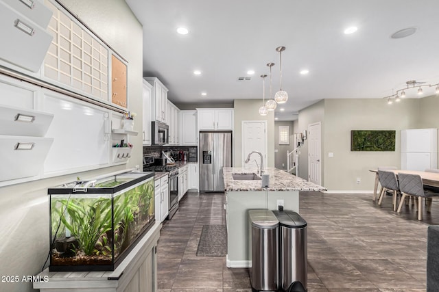 kitchen featuring sink, white cabinetry, hanging light fixtures, stainless steel appliances, and an island with sink