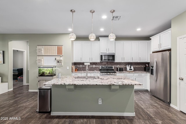 kitchen with a breakfast bar, white cabinets, hanging light fixtures, stainless steel appliances, and a center island with sink