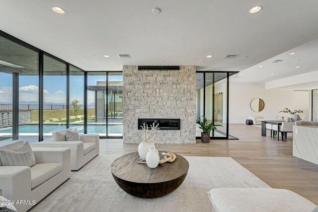 living room with a wall of windows, a stone fireplace, and light wood-type flooring