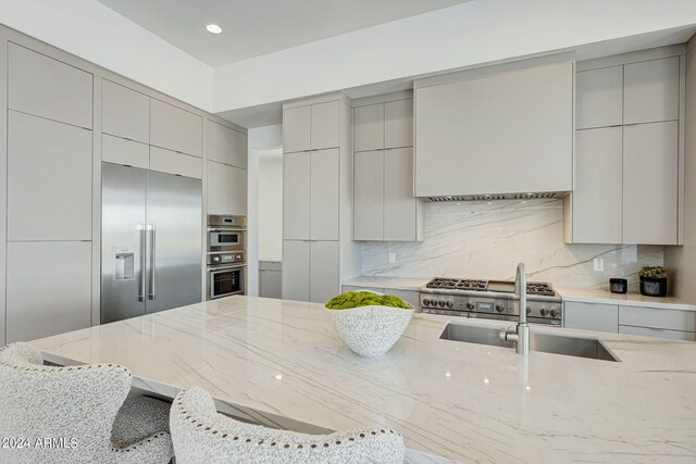 kitchen featuring backsplash, light stone counters, appliances with stainless steel finishes, and a kitchen bar