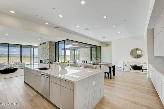 kitchen with floor to ceiling windows, sink, light hardwood / wood-style floors, stainless steel dishwasher, and an island with sink