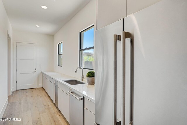 kitchen with sink, high quality fridge, light stone counters, and light hardwood / wood-style flooring