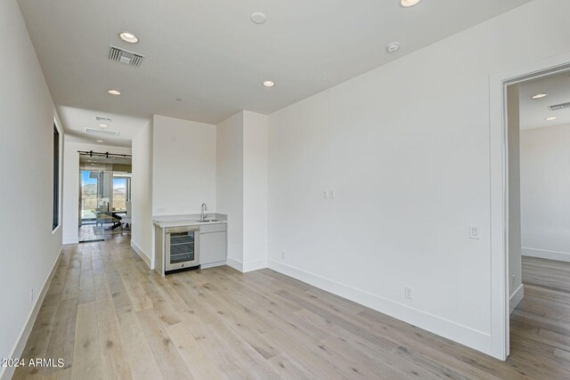 unfurnished living room featuring sink, beverage cooler, and light hardwood / wood-style floors