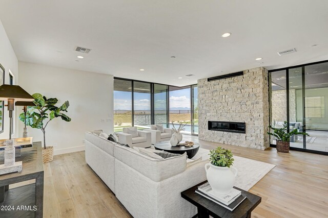 living room with a stone fireplace, a water view, light hardwood / wood-style flooring, and expansive windows