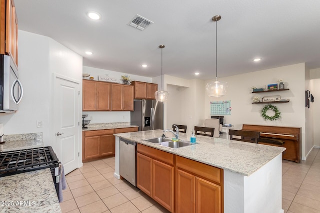 kitchen featuring stainless steel appliances, sink, light tile patterned flooring, hanging light fixtures, and a kitchen island with sink