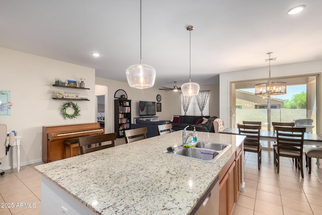 kitchen featuring light stone countertops, hanging light fixtures, a kitchen island with sink, ceiling fan with notable chandelier, and sink